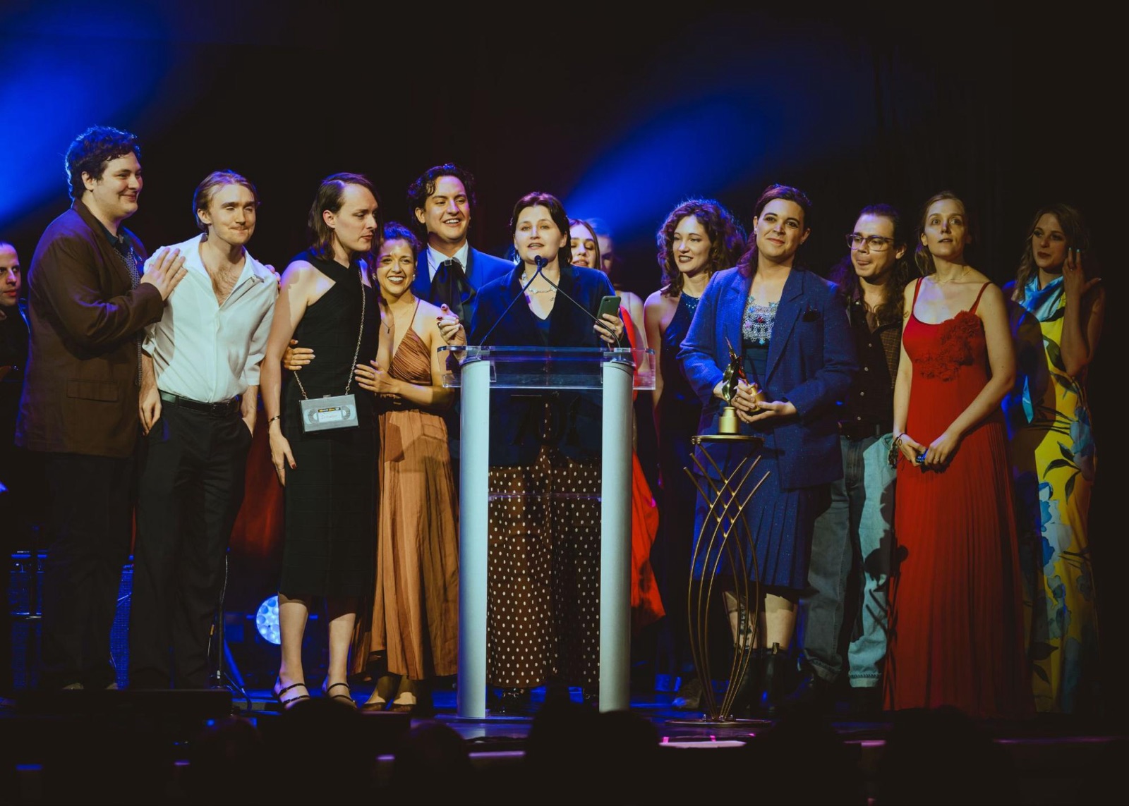 Theater company gathered on stage around a podium at an awards ceremony