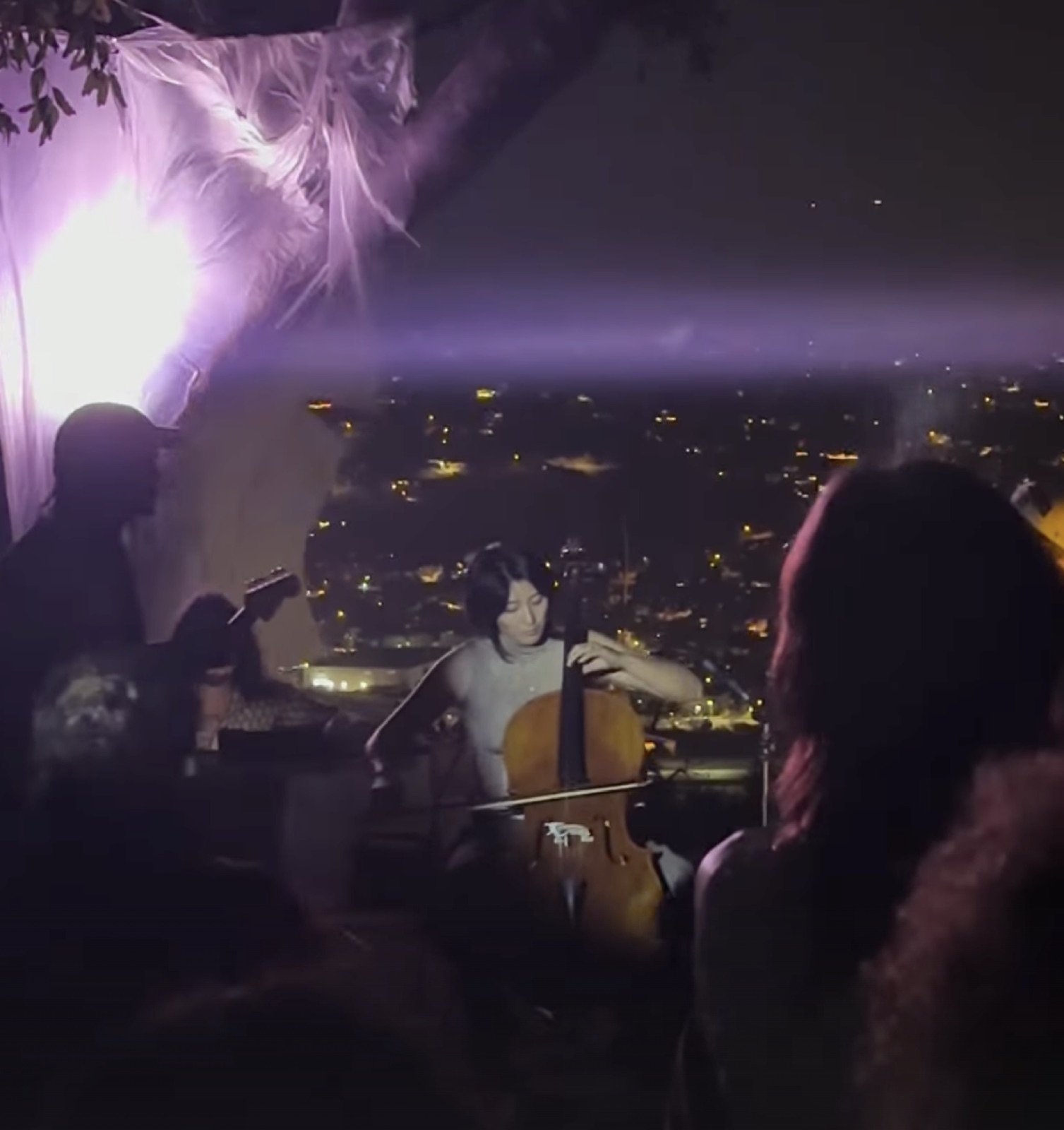 Cellist performing outdoors at night above city lights