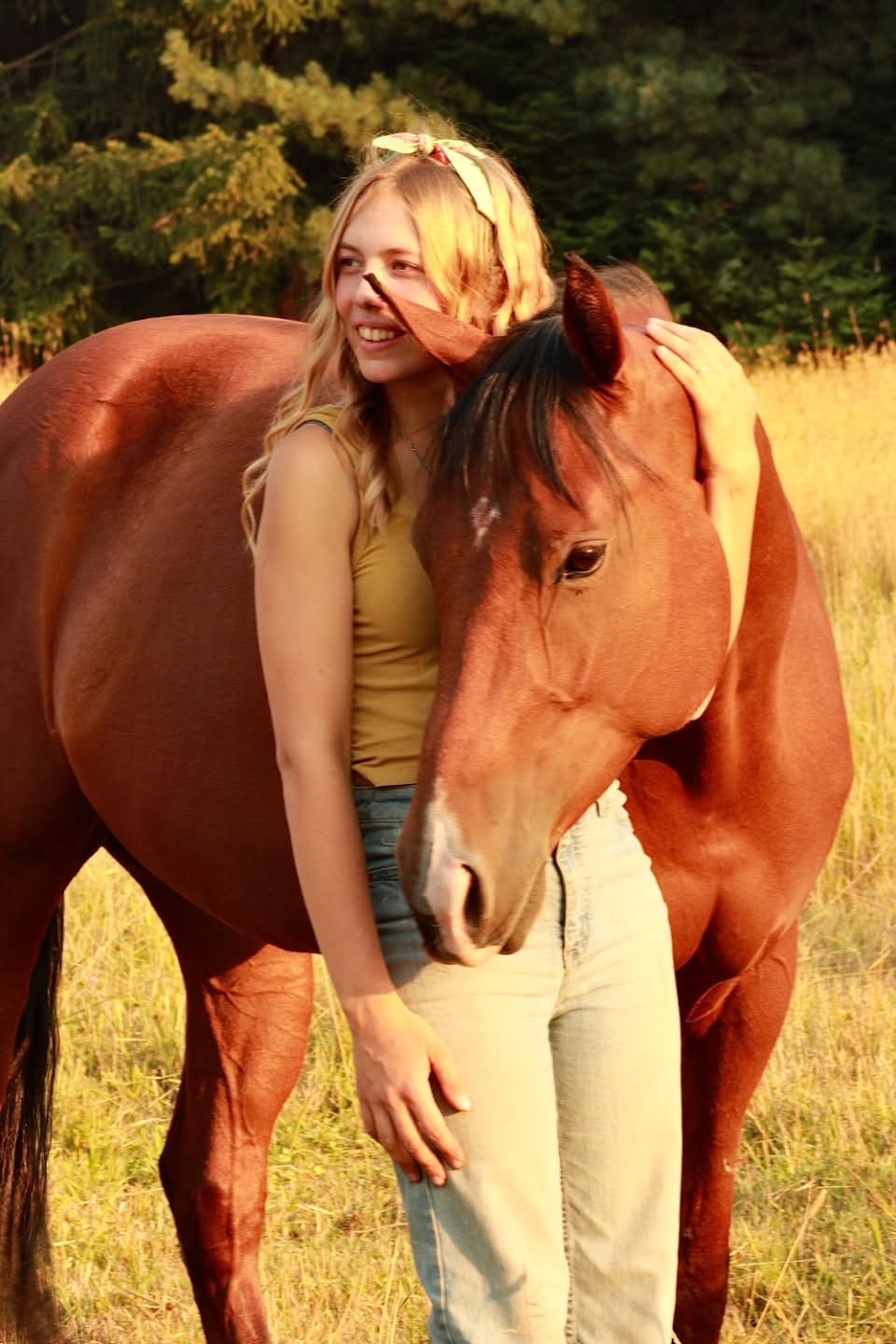 Maryah ’28 smiling as her American Quarter Horse Delilah rests her head against her in a golden pasture