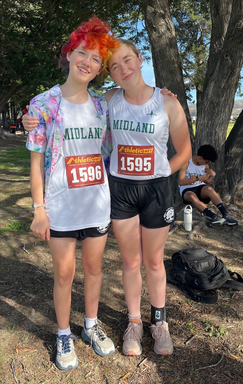 Two Midland cross-country runners in race bibs standing arm in arm