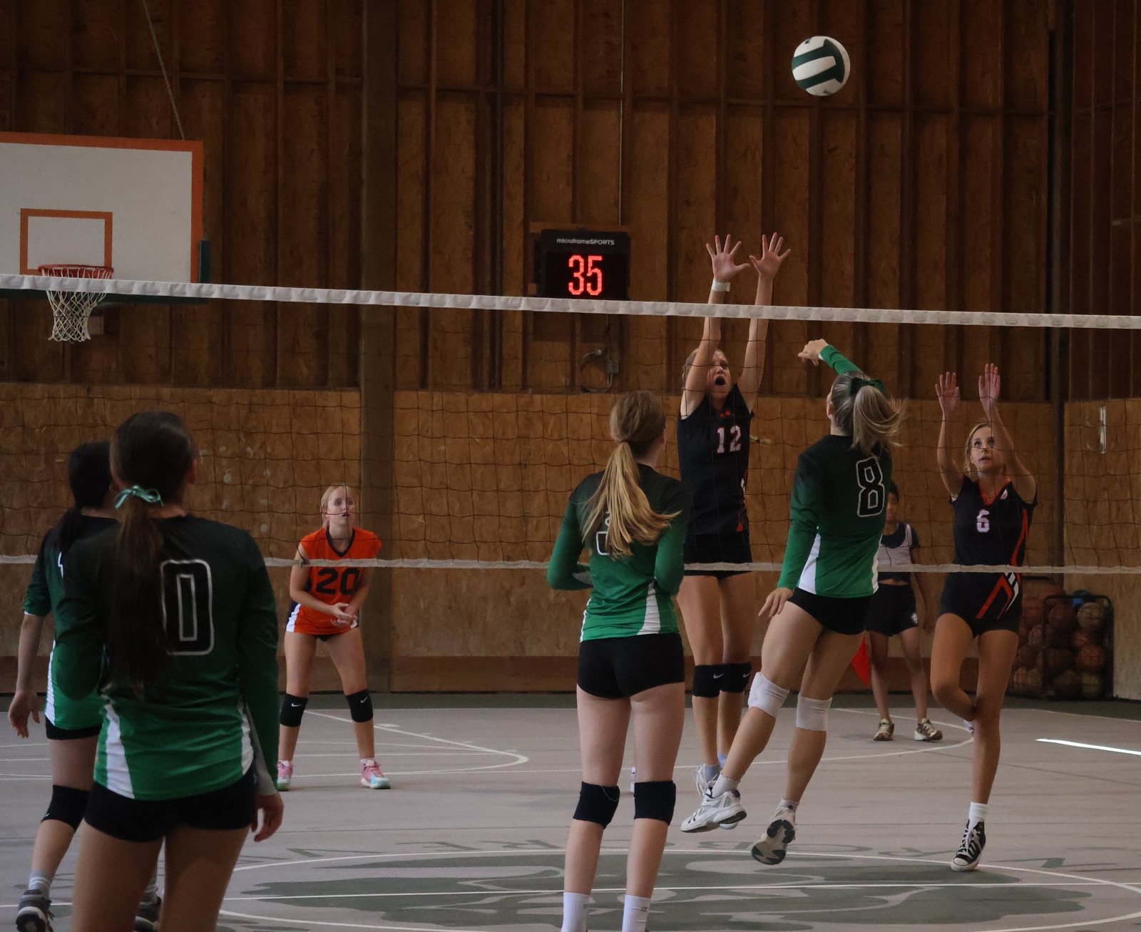 Midland volleyball players in green jerseys playing at the net in the Midland gym